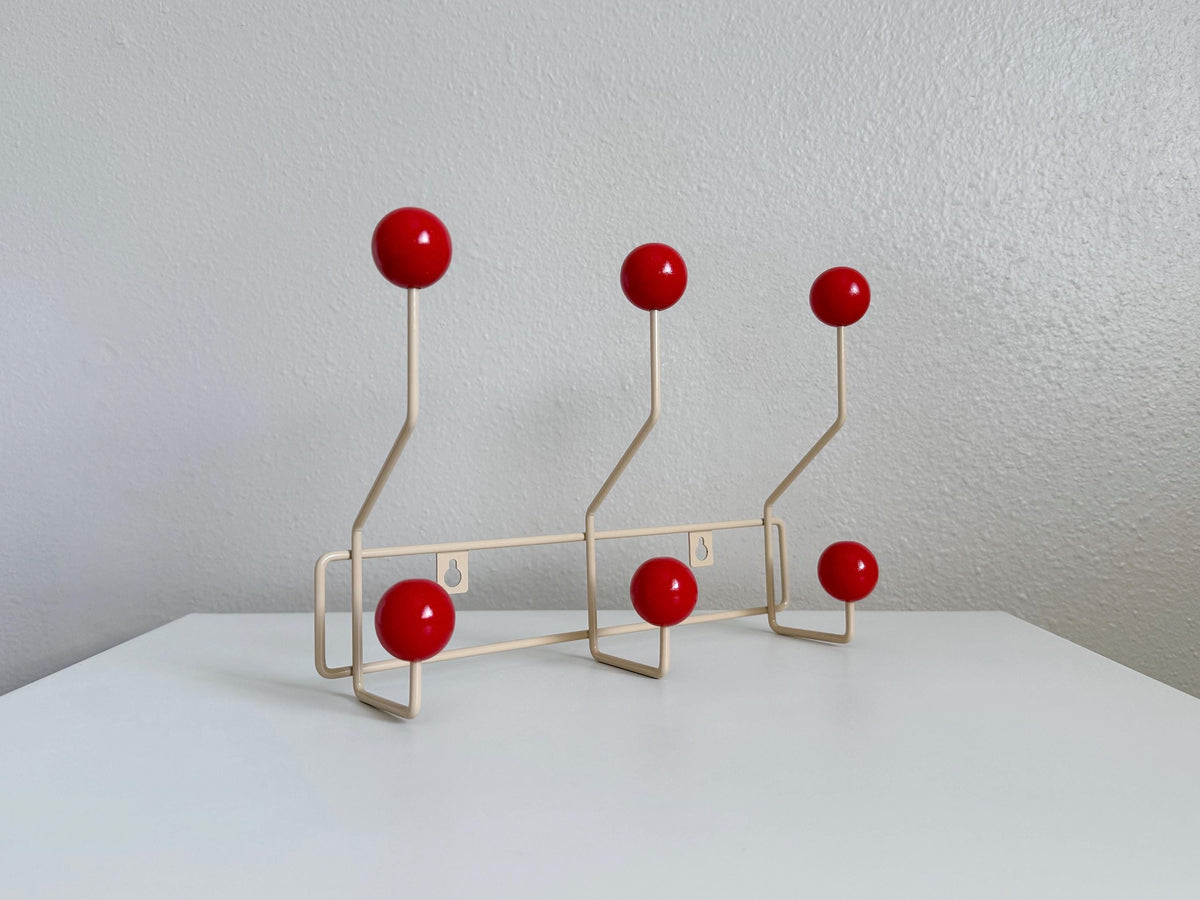 Angled view of a cream-colored coat rack with six red ball hooks.