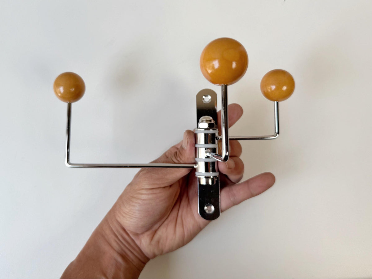 Hand holding a three-arm wall hook with warm brown balls and a silver-colored mounting plate.