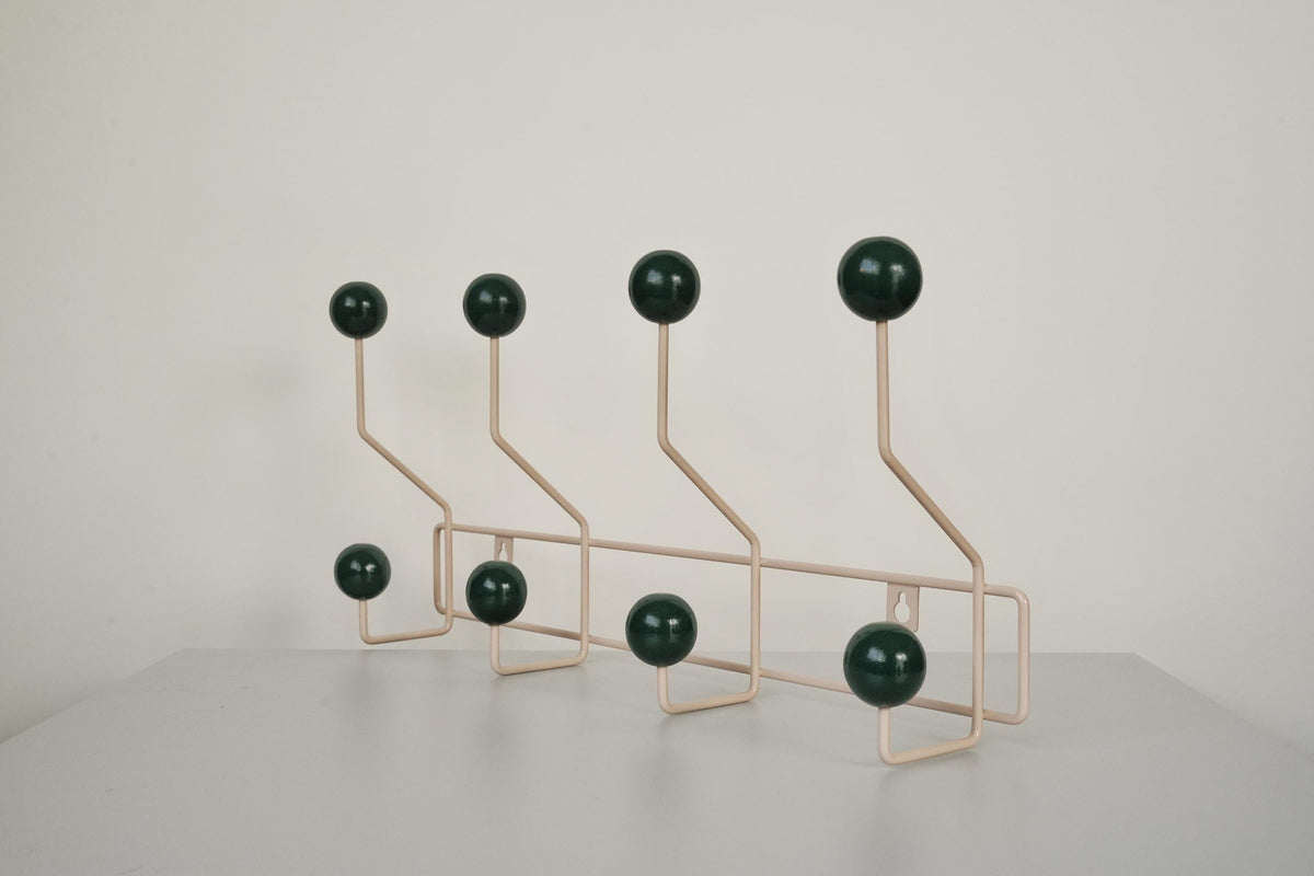 Angled view of a cream-colored coat rack with eight dark green ball hooks.