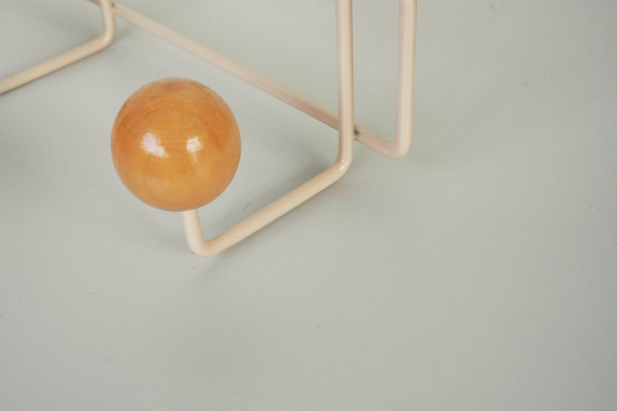 Close-up of a warm brown ball hook on a cream-colored frame.