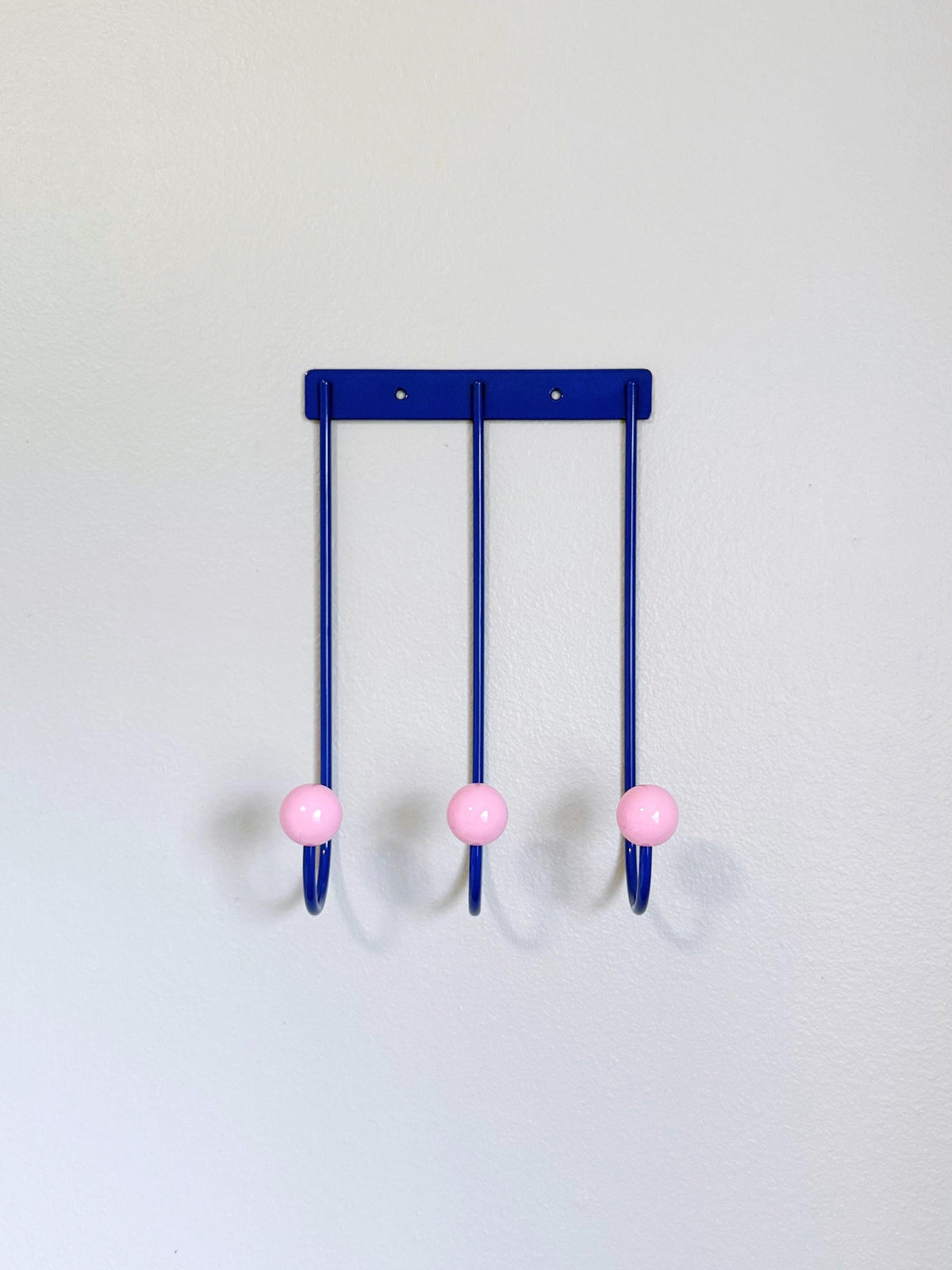 Front view of a blue wall rack with three long curved hooks and pink ball tips.