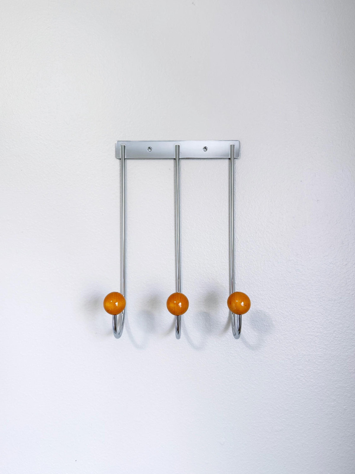 Front view of a silver-colored wall rack with three long curved hooks and golden-brown ball tips.