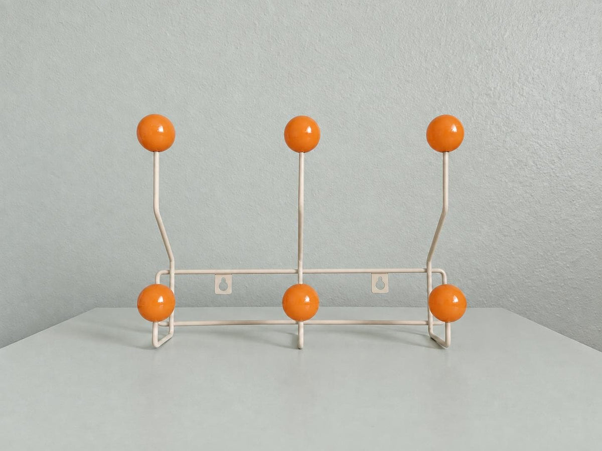 Front view of a cream-colored coat rack with six orange ball hooks.