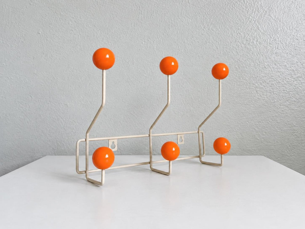 Angled view of a cream-colored coat rack with six orange ball hooks.
