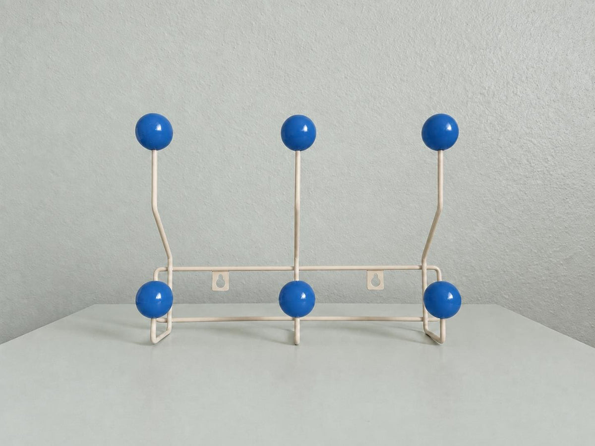 Front view of a cream-colored coat rack with six blue ball hooks.