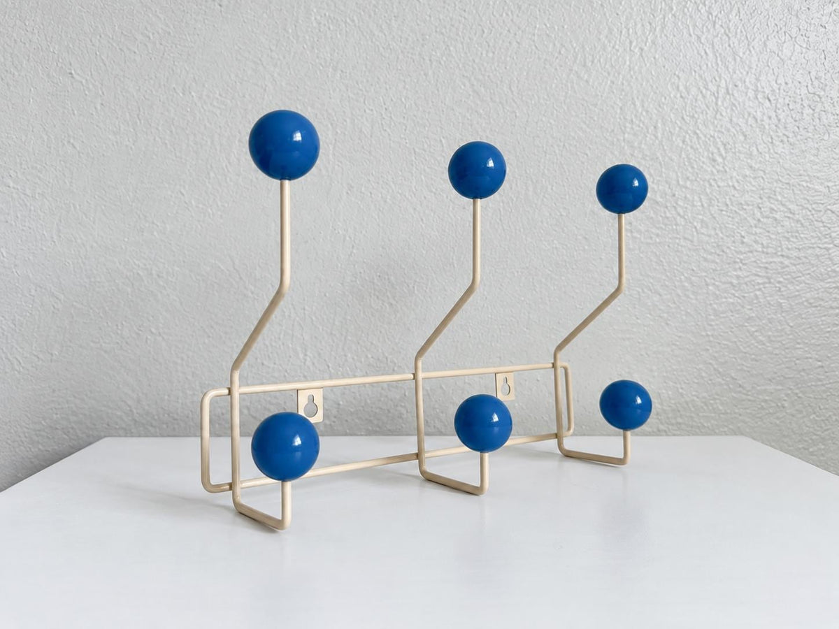 Angled view of a cream-colored coat rack with six blue ball hooks.