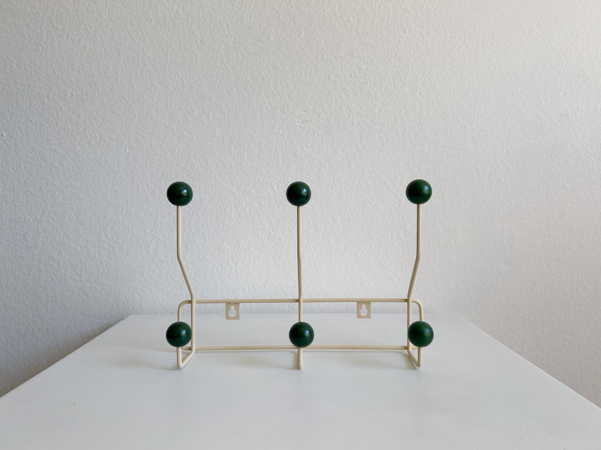 Front view of a cream-colored coat rack with six dark green ball hooks.