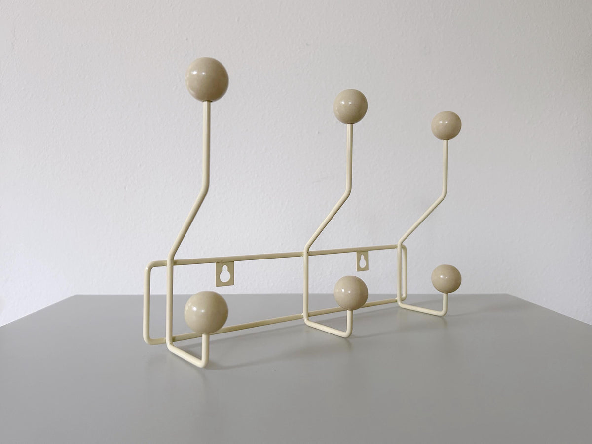 Angled view of a cream-colored coat rack with six cream ball hooks.