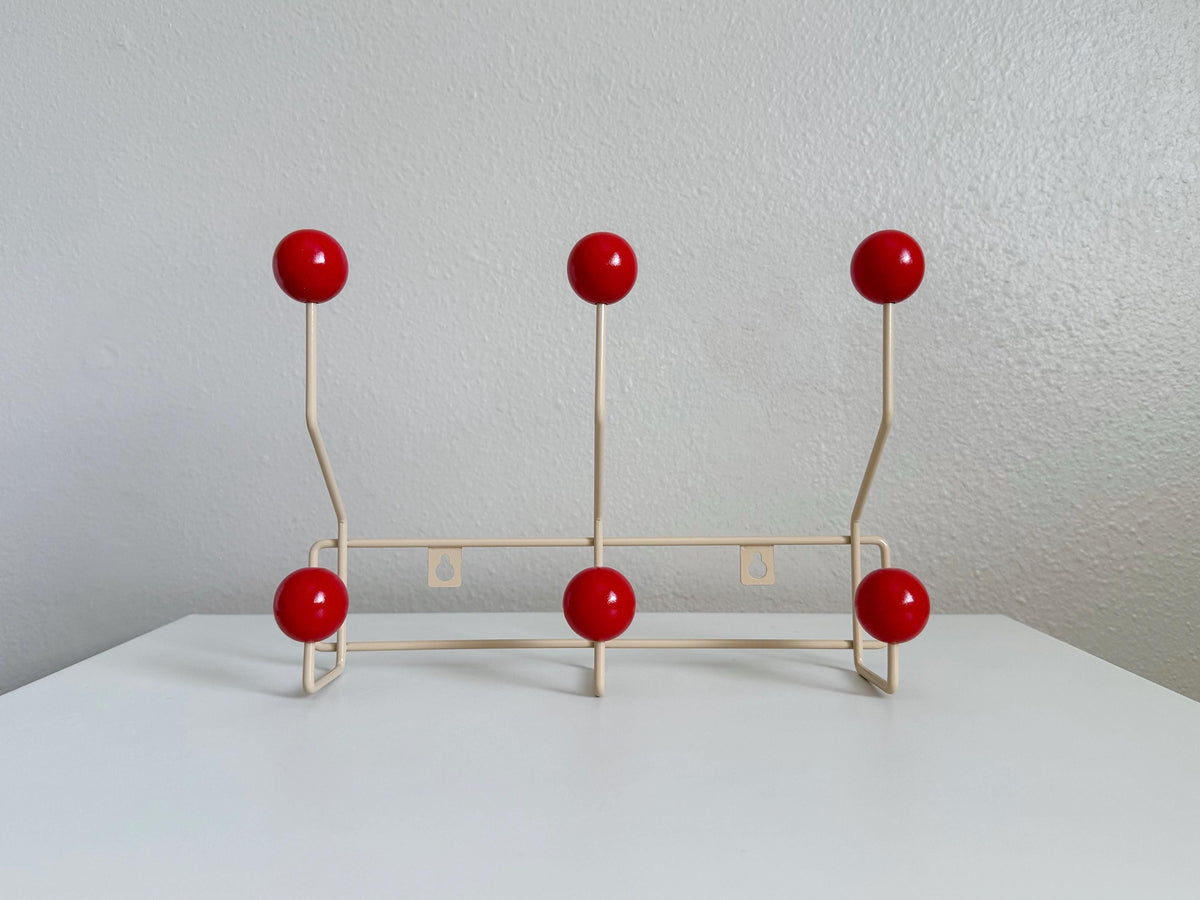 Front view of a cream-colored coat rack with six red ball hooks.