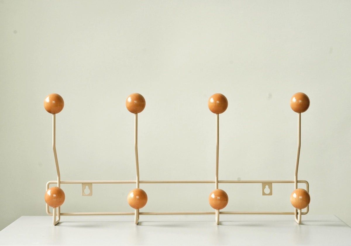 Front view of a cream-colored coat rack with eight warm brown ball hooks.