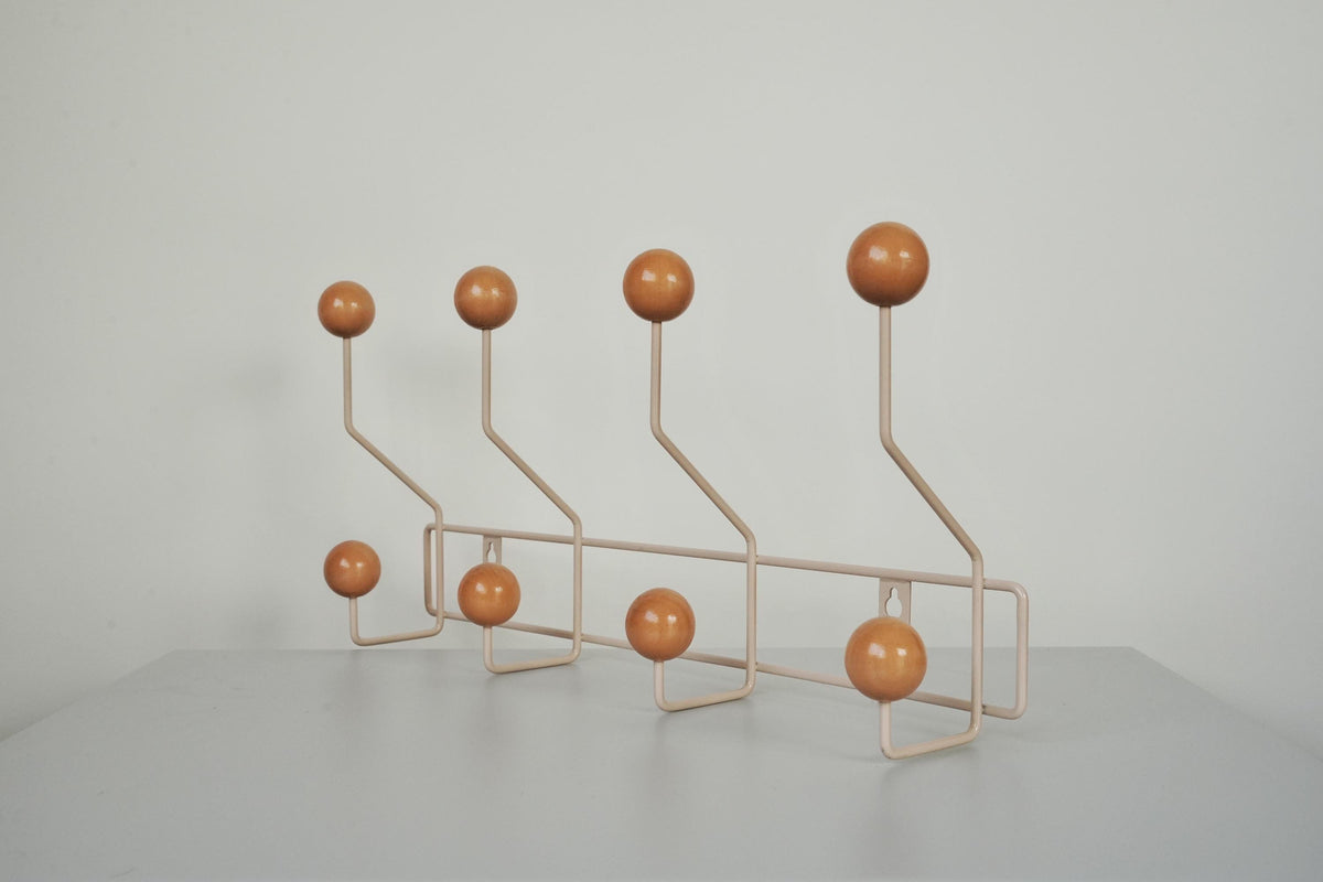 Angled view of a cream-colored coat rack with eight warm brown ball hooks.
