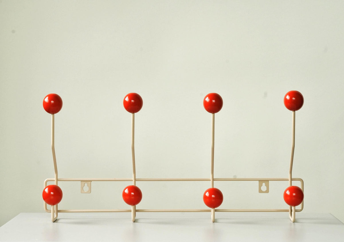 Front view of a cream-colored coat rack with eight red ball hooks.