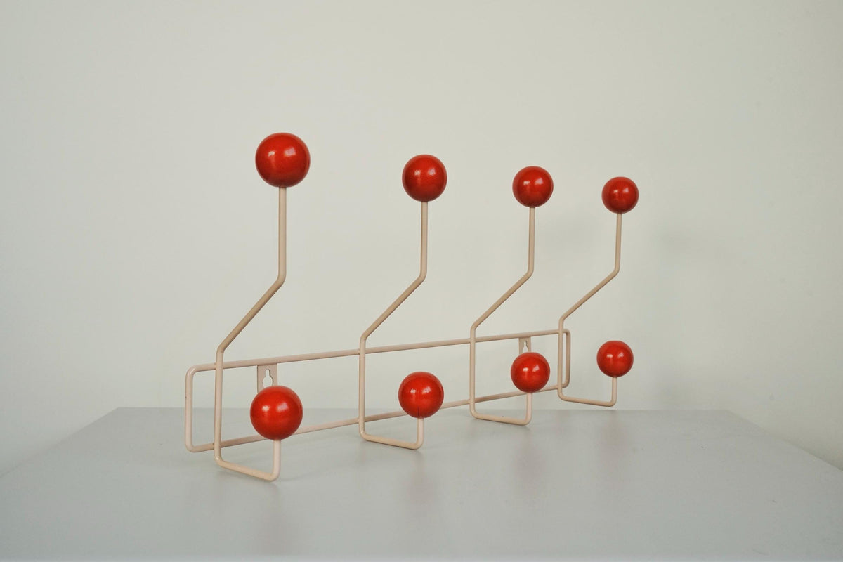 Angled view of a cream-colored coat rack with eight red ball hooks.