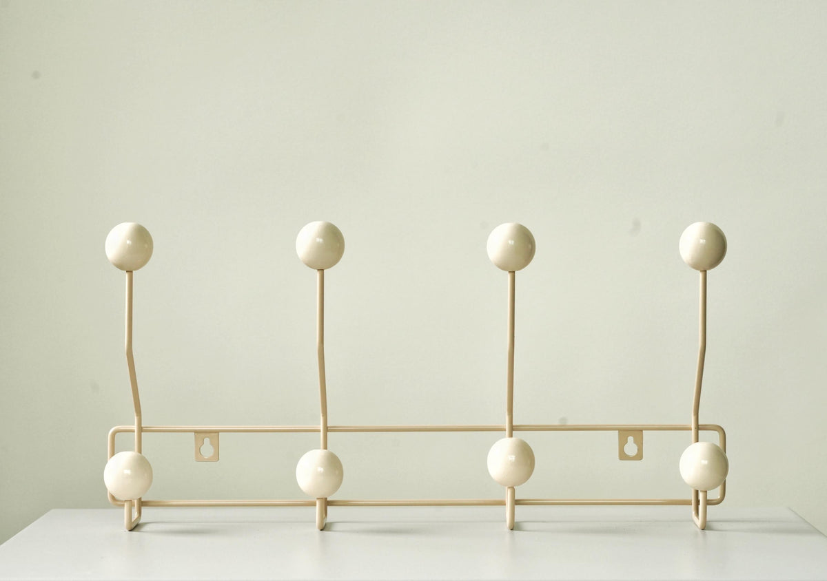Front view of a cream-colored coat rack with eight cream ball hooks.