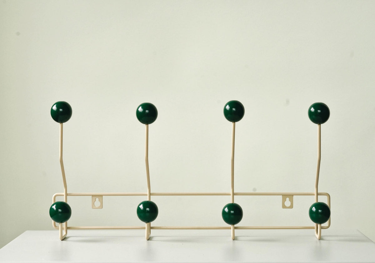 Front view of a cream-colored coat rack with eight dark green ball hooks.