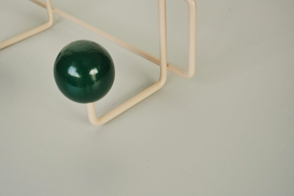 Close-up of a dark green ball hook on a cream-colored frame.