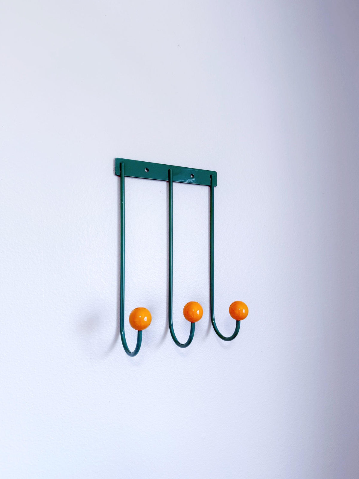 Angled view of a green wall rack with three long curved hooks and orange ball tips.