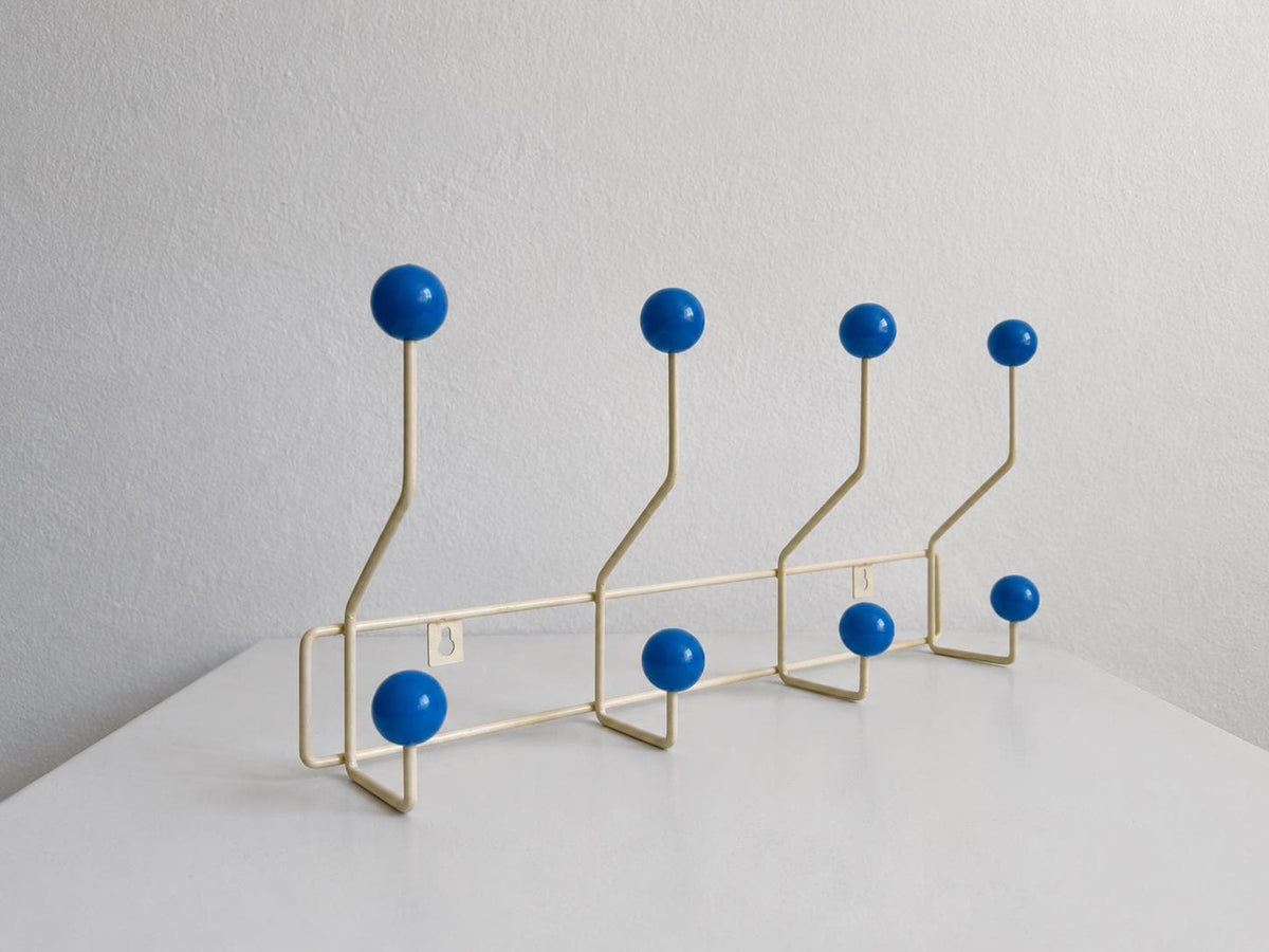 Angled view of a cream-colored coat rack with eight blue ball hooks.