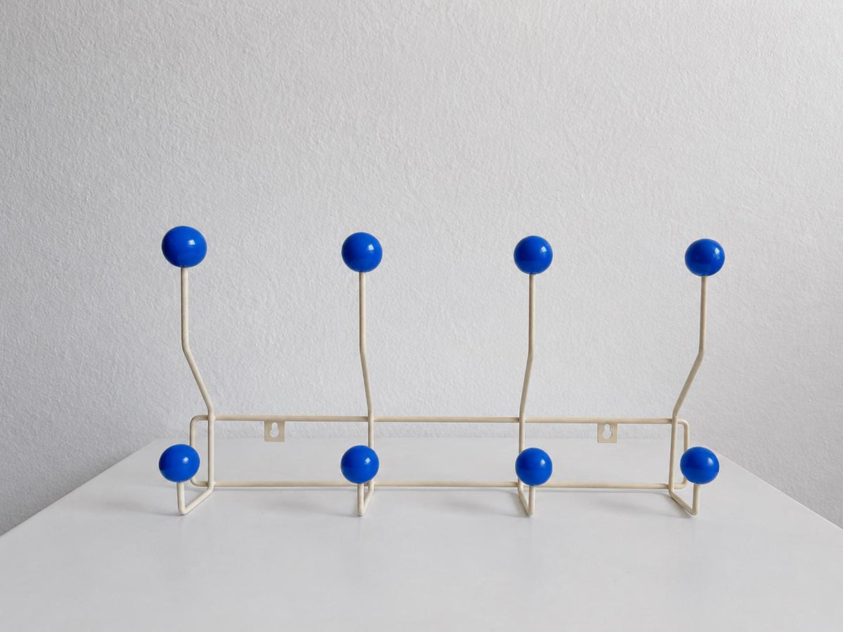 Front view of a cream-colored coat rack with eight blue ball hooks.