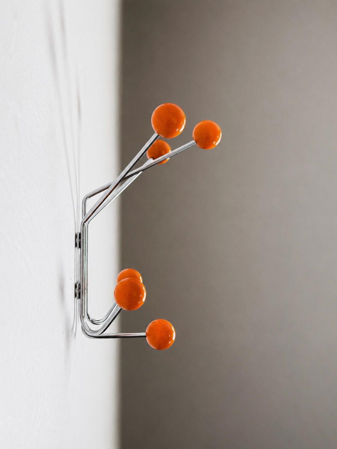 Side view of an orange ball hook rack mounted on a white wall.