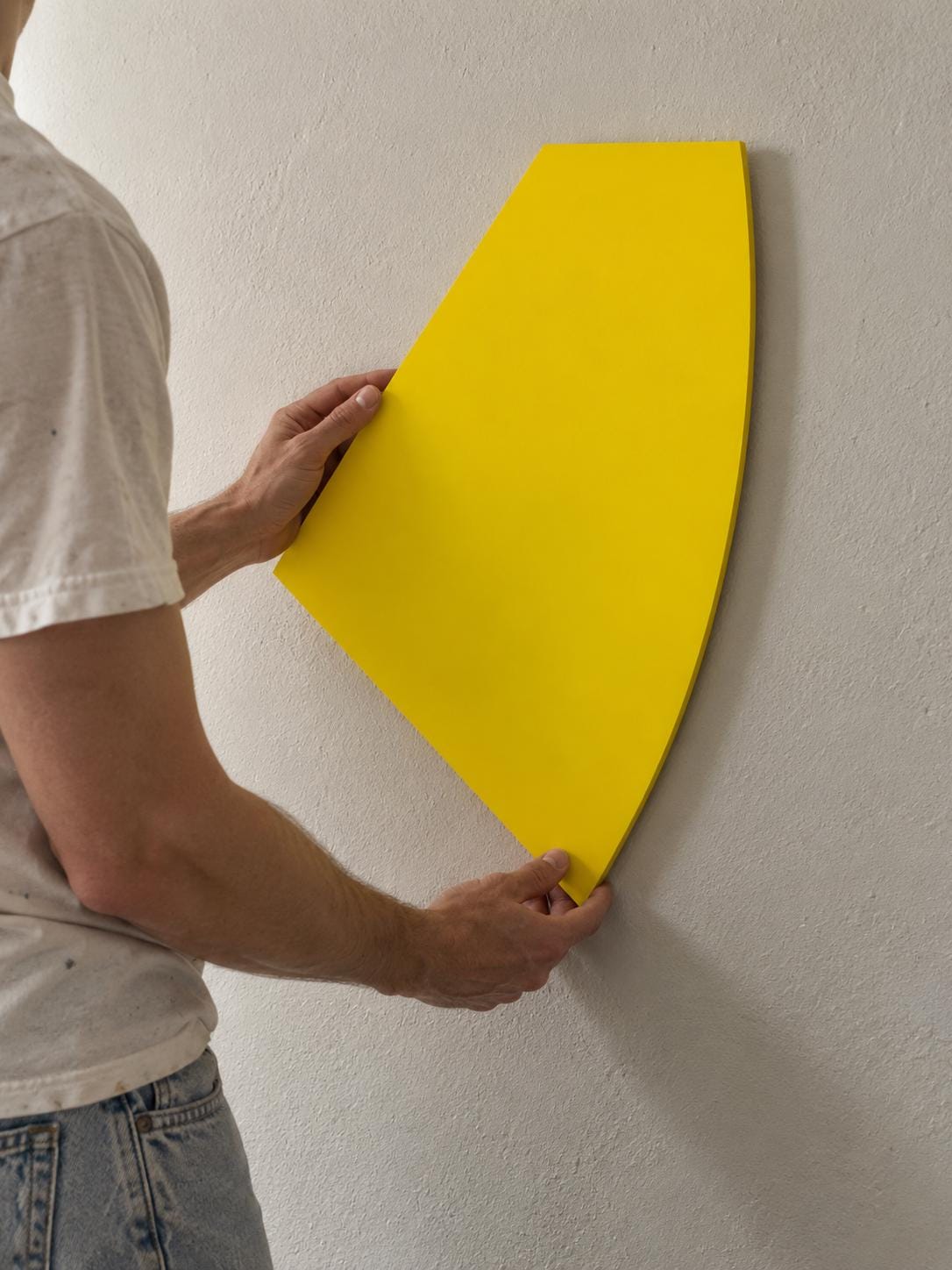 Person positioning a yellow curved-edge wall panel on a cream wall.