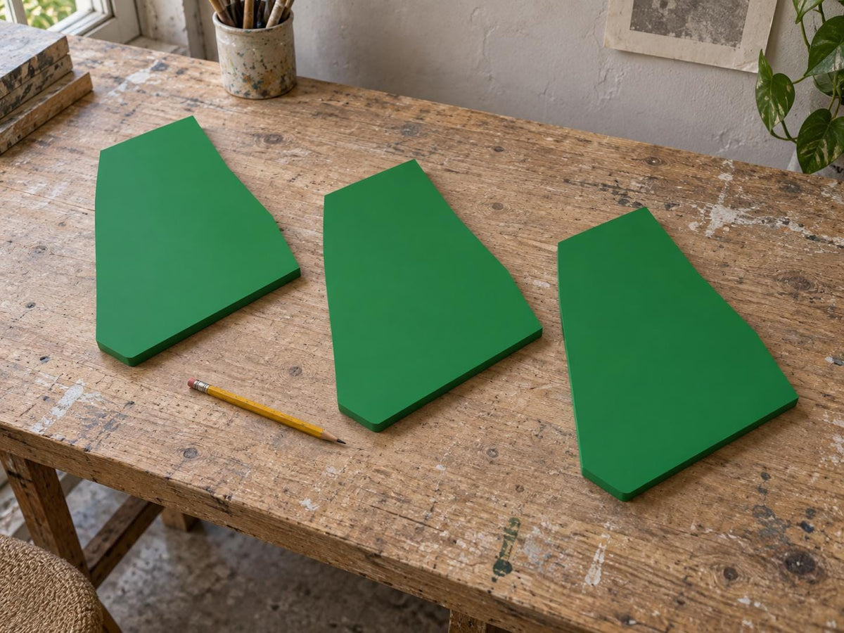 Three green irregular panels on a worktable beside a pencil.